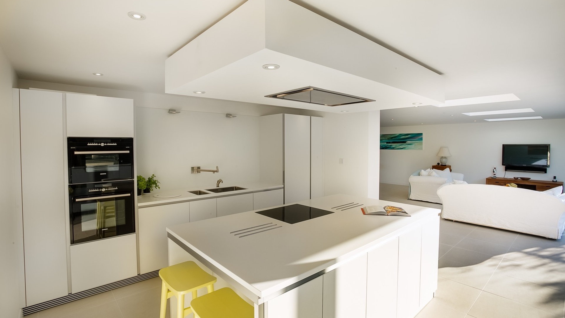 Open-plan white kitchen with island and living area beyond